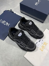Load image into Gallery viewer, Pair of black Dior trainers with white piping, displayed with original navy box, dust bag, white care pouch, and Dior documentation cards.