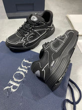 Load image into Gallery viewer, Pair of black Dior trainers with white piping, displayed with original navy box, dust bag, white care pouch, and Dior documentation cards.