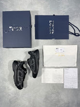 Load image into Gallery viewer, Pair of black Dior trainers with white piping, displayed with original navy box, dust bag, white care pouch, and Dior documentation cards.