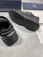 Load image into Gallery viewer, Pair of black Dior trainers with white piping, displayed with original navy box, dust bag, white care pouch, and Dior documentation cards.