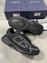 Load image into Gallery viewer, Pair of black Dior trainers with white piping, displayed with original navy box, dust bag, white care pouch, and Dior documentation cards.